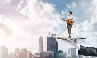 Fototapeta na wymiar Attractive businesswoman on metal tray playing acoustic guitar against cityscape background