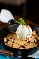 Traditional english crumble cake with apples and scoop of vanilla ice cream served in cast iron baking pan close up