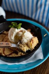 Traditional english crumble cake with apples and scoop of vanilla ice cream served in cast iron baking pan close up