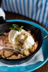 Traditional english crumble cake with apples and scoop of vanilla ice cream served in cast iron baking pan close up