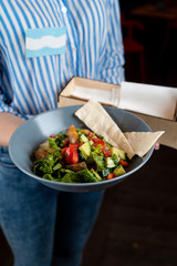 Waitress is holding a plate with warm seasonal salad with baked jacket potato, served with flat bread