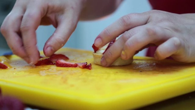 Cook making a row of vanilla and strawberry mini tarts for a sweet buffet  