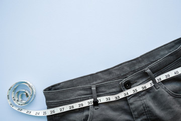 White measure tape with dark gray jeans on light pastel blue table. Men diet. Mock up for healthy...