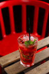 Red strawberry lemonade with ice and fresh mint served outdoors on a summer terrace
