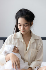 Mother carrying her baby in white bed room. Cute newborn baby sleeping in mother 's arm. Housewife and mother 's day concept.