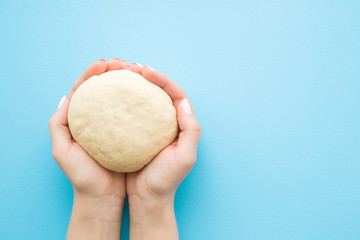Fresh raw dough in woman's hands. Ready for baking. Closeup. Point of view shot. Empty place for text on light pastel blue table.