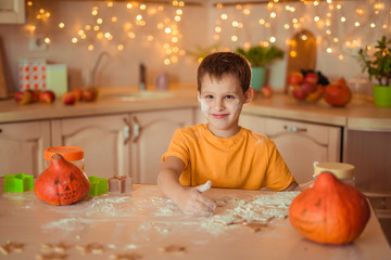 7 happy cute baby sitting at a table in the kitchen waiting for Halloween and preparing a gingerbread cookie