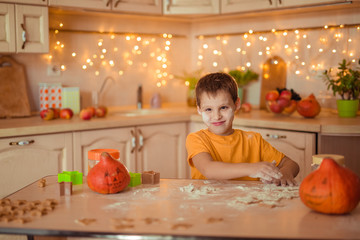 7 happy cute baby sitting at a table in the kitchen waiting for Halloween and preparing a gingerbread cookie