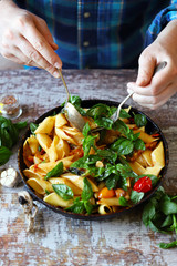 Chef mixes pasta with basil and spices in a pan. Appetizing pasta in a pan with tomatoes, basil and spices. One pan pasta. Italian vegan pasta. Selective focus. Macro.