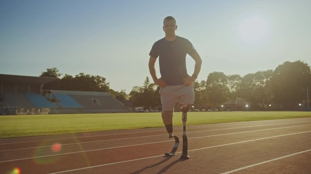 Athletic Disabled Fit Man with Prosthetic Running Blades is Posing During a Training on an Outdoor Stadium on a Sunny Afternoon. Amputee Runner Standing on a Track. Motivational Sports Footage.