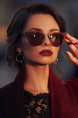 Closeup portrait of young elegant woman wearing sunglasses. Pretty girl with hairstyle and makeup. Outdoor portrait. Sunset light.