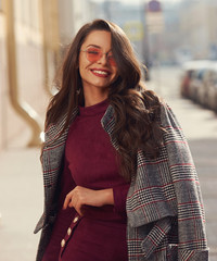 Outdoor sunny portrait of young elegant stylish woman in burgundy color dress, gray coat and...