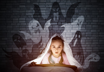 Scared little girl reading book in bed