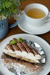 Banoffee pie with hot tea, whipped cream, chocolate, on wood table