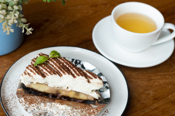 Banoffee pie with hot tea, whipped cream, chocolate, on wood table
