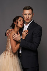 Portrait of young couple in love posing against gray backgound in studio dressed in classic clothes. Pretty woman in luxury dress tender hugging with handsome man