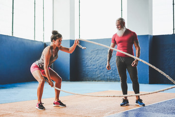 Fit woman training with battle rope inside gym - Personal trainer motivating a female athlete doing...