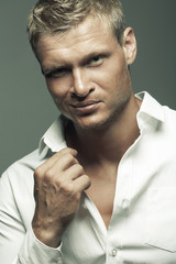 Male fashion, beauty concept. Portrait of brutal young man with short wet blond hair wearing white shirt, posing over gray background. Classic style. Close up. Hands crossed. Studio shot