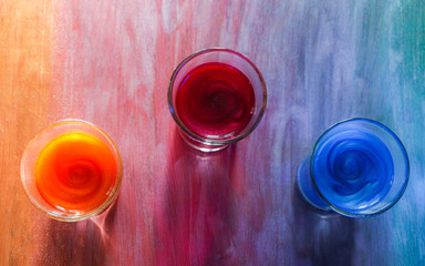 Colored drinks with sparkles in glasses on a rainbow wooden table