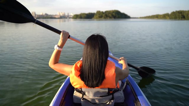 A girl floats in a kayak boat on the river and rowing an oar