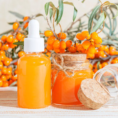 Cosmetology, traditional alternative medicine, herbal medicine, natural sea buckthorn vegetable oil in a glass jar on a table background, healthy juice, branches with a harvest of fresh ripe berries