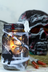 Jar filled with orange string lights in spooky room full in a black jar with a web and a spider on a dark background