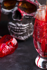 Halloween bloody glass with tomato juice and a human skeleton face as cup on black background