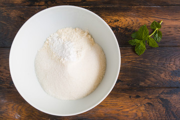 Dough making, flour, sugar and baking powder in white bowl. Wooden rustic table, top view