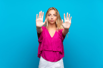 Blonde young woman over isolated blue background making stop gesture and disappointed