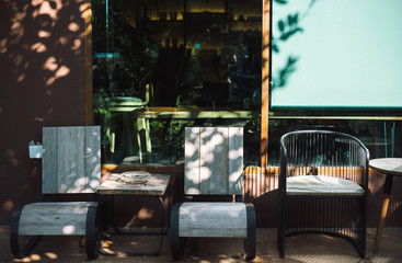 close up wooden chairs beside glass wall with sun light and leave shadow