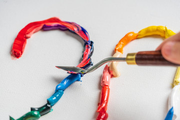 Bright squeezed oil paints on canvas. Girl draws with a palette knife. The process of creating a picture.