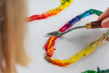 Bright squeezed oil paints on canvas. Girl draws with a palette knife. The process of creating a picture.