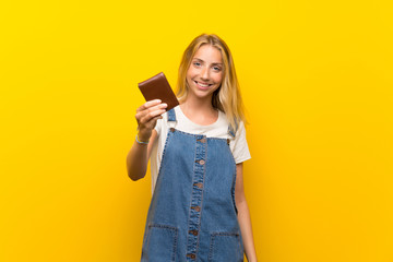 Blonde young woman over isolated yellow background holding a wallet