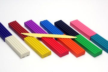 Multicolored set of plasticine sticks and sculptural knife on white background.