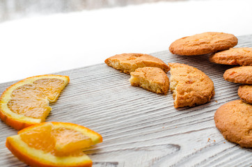 Round orange biscuits with colorful candied fruits and a slice of juicy orange lying on a wooden table against the background of winter forest