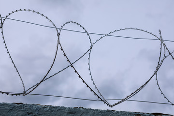Turns of barb wire on top of aged fence, close up, soft focus. Old concrete wall with barbed wire against dark cloudy sky