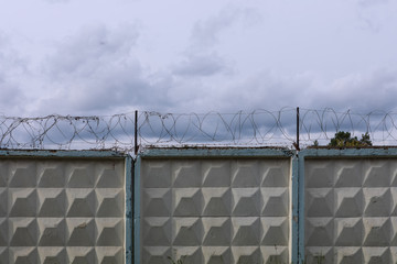 Fototapeta premium Old concrete wall with barbed wire against dark cloudy sky. Tangle barb wire on top of aged fence
