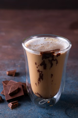 Glass cup of coffee latte with chocolate on stone dark table