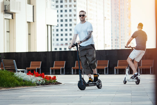Two handsome men riding electric kick scooters at beautiful cityscape.