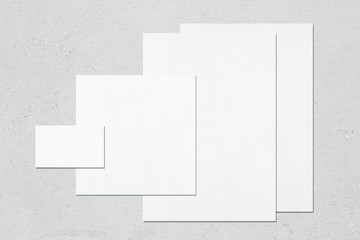 Empty white office stationery mockups with soft shadows on neutral light grey concrete background. Flat lay, top view