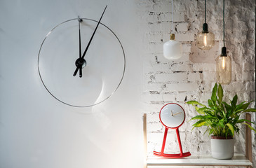 Clock hanging on the white wall and red design clock with plant on the shelf. Lamps illuminate the interior of office.. Copy space.