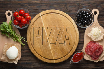 Pizza word on blackboard. Italian cooking. Pizza board and pizza ingredients on a wooden table.