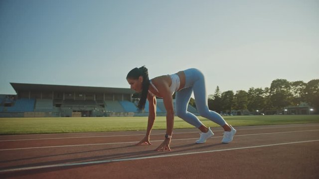 Beautiful Fitness Woman in Light Blue Athletic Top and Leggings is Starting a Sprint Run in an Outdoor Stadium. She is Running on a Warm Summer Day. Athlete Doing Her Sports Practice.