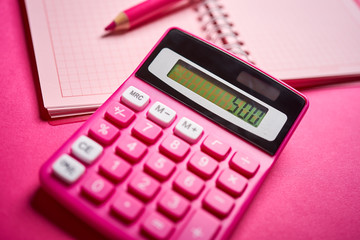 Closeup of calculator and notebook with pencil on pink desk
