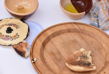 piece of bread on a wooden dish, next to half-empty clay cups with honey and olive oil