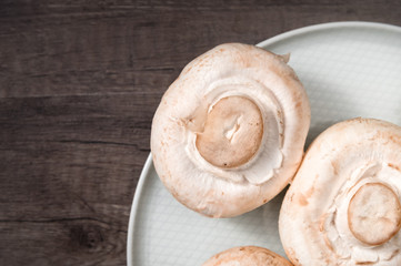 Close-up of white mushrooms on a white plate on a dark wooden table. Vegetarian healthy food