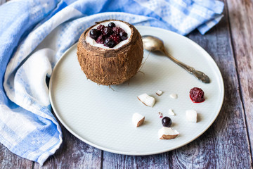 Berry dessert with yogurt in a cup of coconut on a wooden background. Blackberries, raspberries, blueberries, black currants. Blue napkin