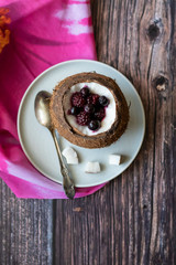 Berry dessert with yogurt in a cup of coconut on a wooden background. Blackberries, raspberries, blueberries, black currants. Pink napkin
