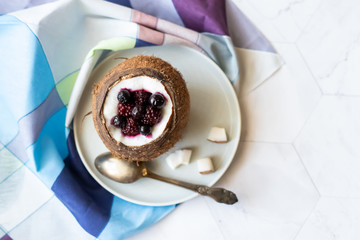 Berry dessert with yogurt in a cup of coconut on a light background. Blackberries, raspberries, blueberries, black currants. Blue napkin