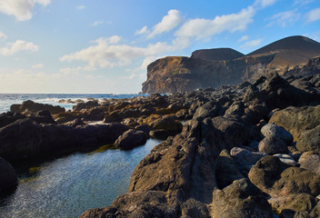 Fototapeta premium Coastal view of volcanic rocks and cliffs at Ponta Dos Capelinhos, the westernmost point of Europe, submerged in an eruption from under the atlantic ocean in 1957, on Faial island, Azores.